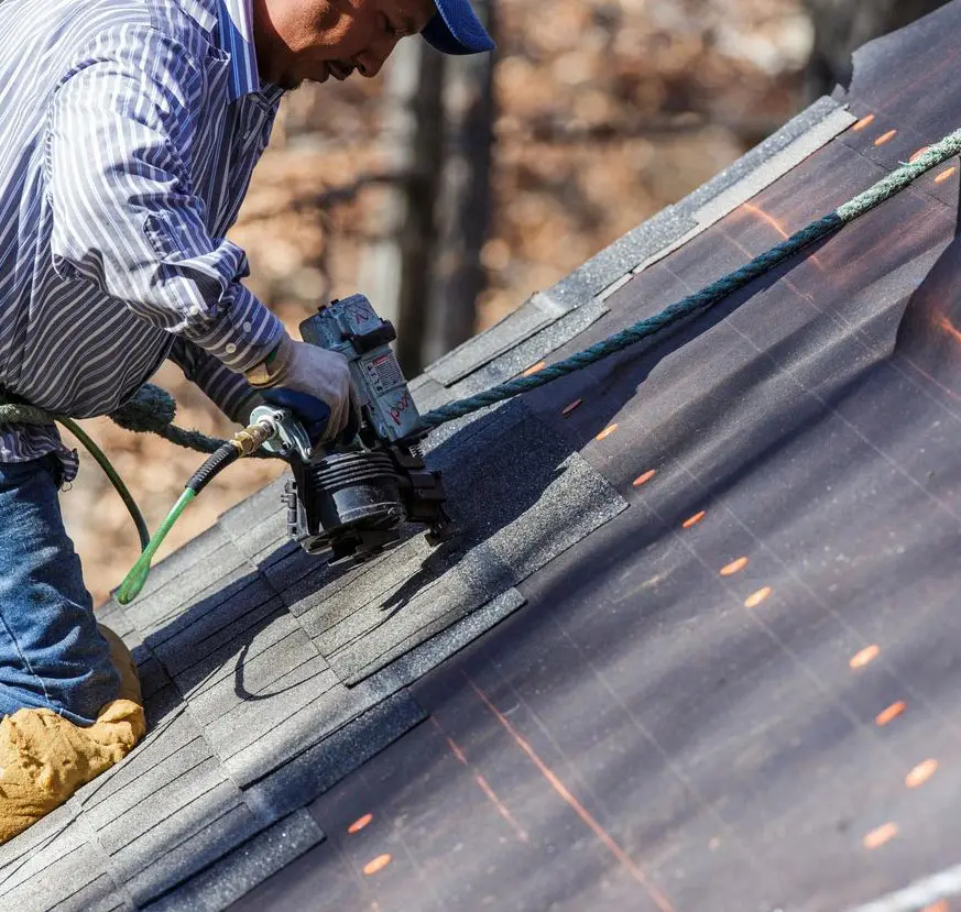 Carpenter uses nail gun to attach asphalt shingles to roof