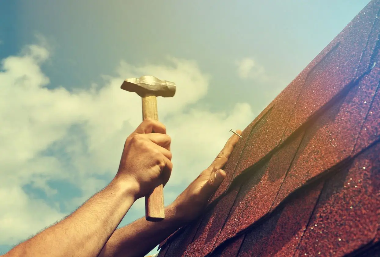 Roof repairs on background workers hands with hammer , focus on roof